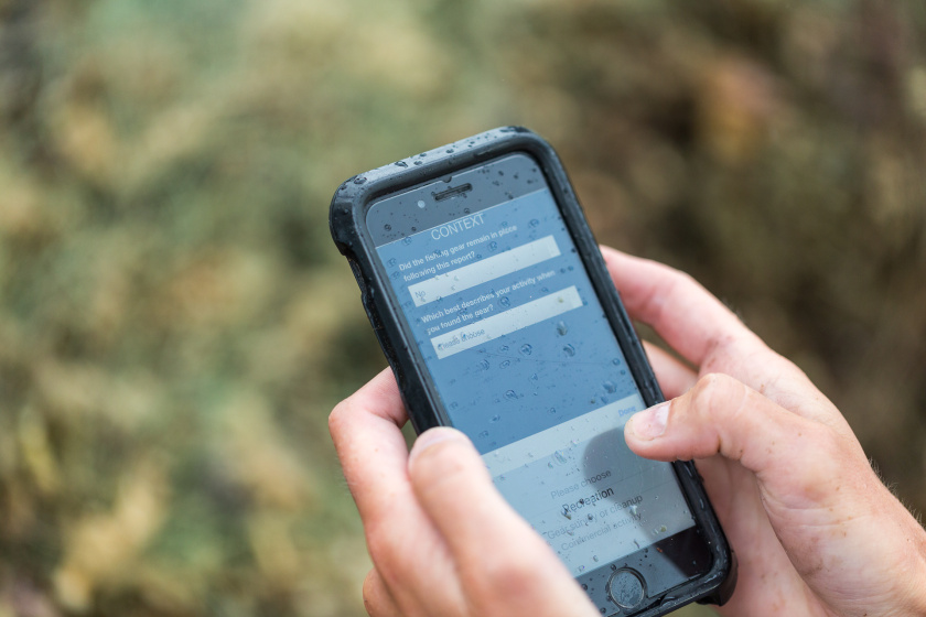 A photo of someone using the Global Ghost Gear Initiative App on a smartphone in the rain.