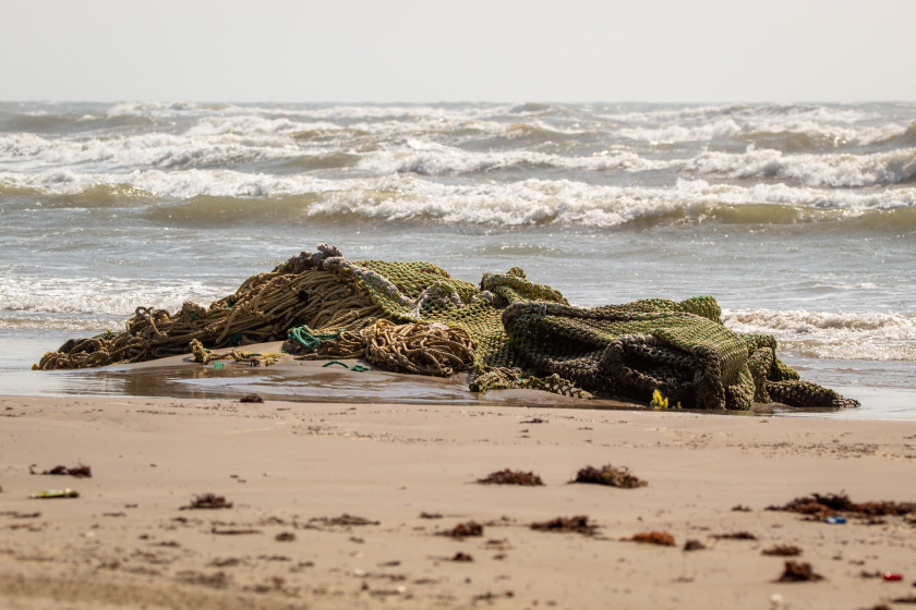A discarded fishing net - known as 'ghost gear' - on a beach with the sea in the background.