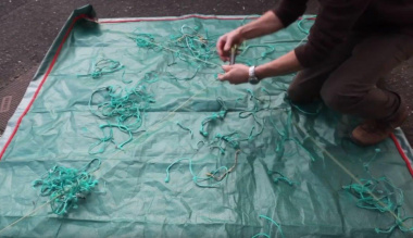 A fisherman collecting net cuttings on a tarpaulin.